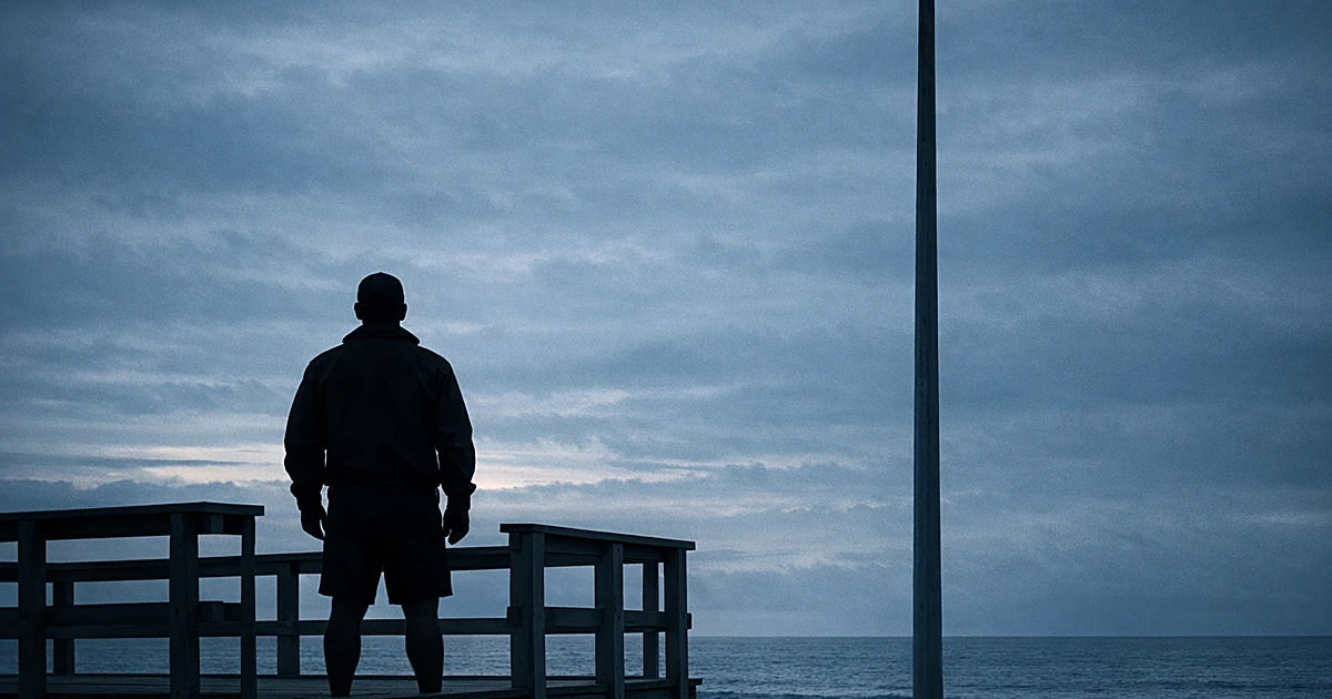 Silhouetted lifeguard on tower with empty flagpole against overcast sky and ocean