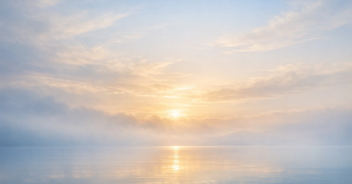 Soft morning light filtering through misty clouds over a peaceful horizon in warm and cool tones