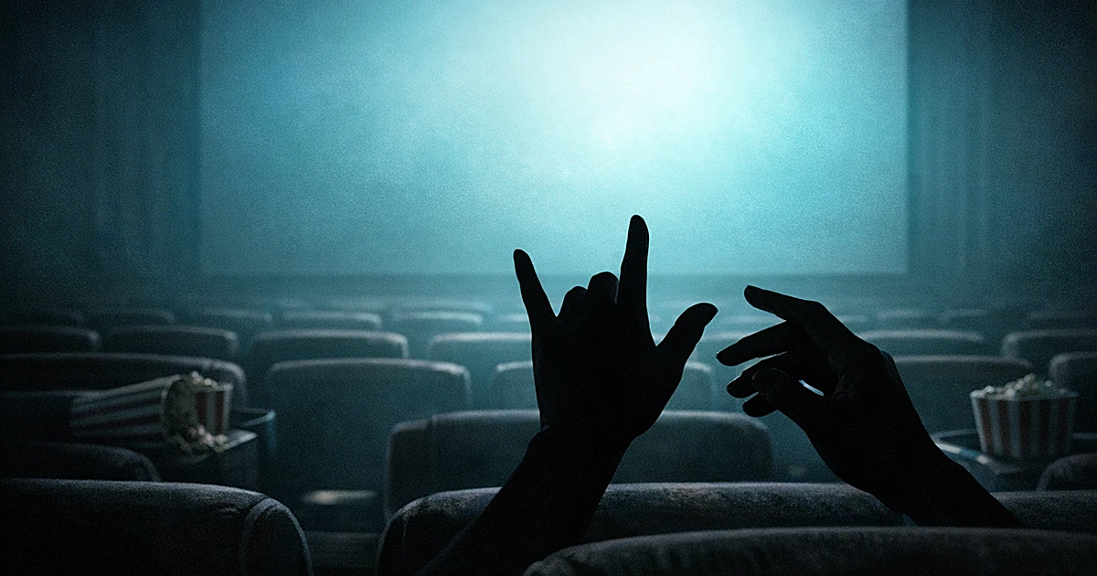 Empty movie theater with hands signing in silhouette against glowing screen, scattered popcorn containers on seats