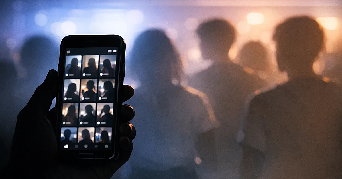 Silhouetted hand holding smartphone showing video grid interface with blurred figures in background